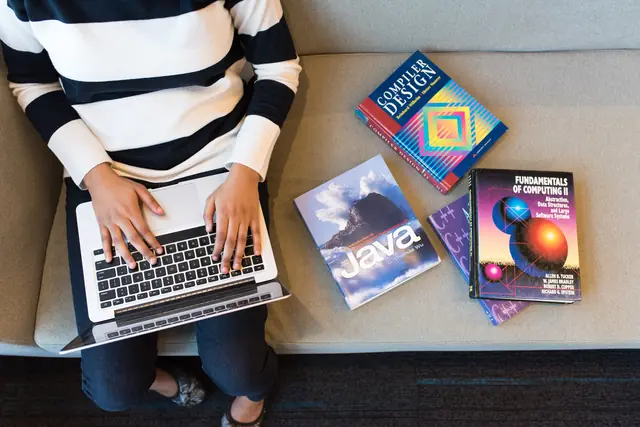 Une élève programme sur son ordinateur à côté de livres d’informatique
