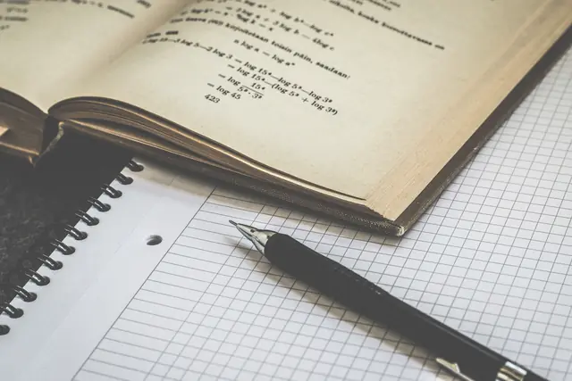 An open mathematics book with equations, a notebook and a pen
